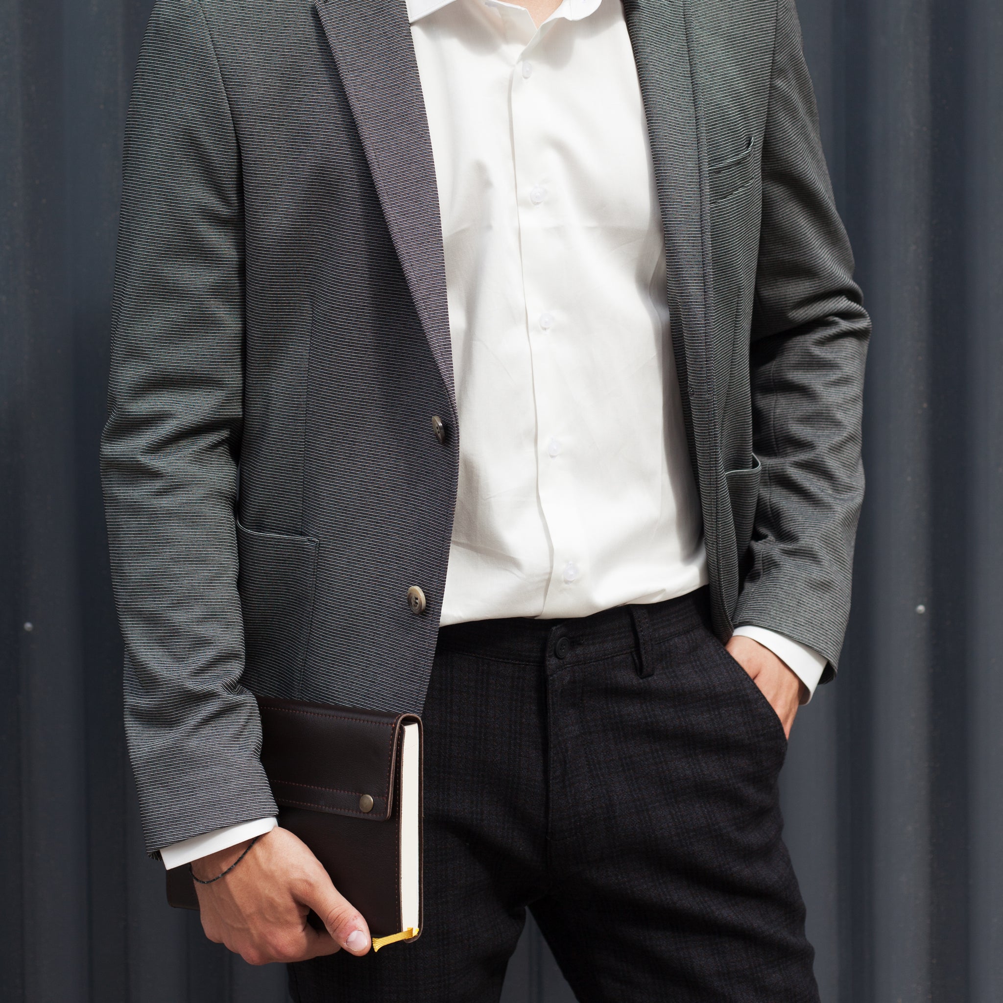 Person wearing a gray blazer and white shirt, holding a book against a plain background