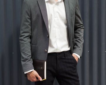 Person wearing a gray blazer and white shirt, holding a book against a plain background