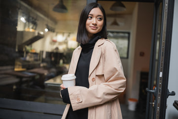 Woman in a beige coat holding a coffee cup outside a cafe.